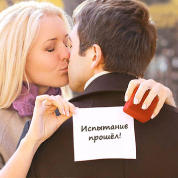 Девушка целует жениха и держит лист бумаги за спиной  
