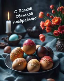 Красивые пасхальные яйца на тарелке и зажжённая свеча с красными цветами
