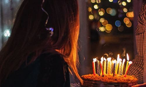 Девушка задувает торт на свой день рождения свечи стоит спиной